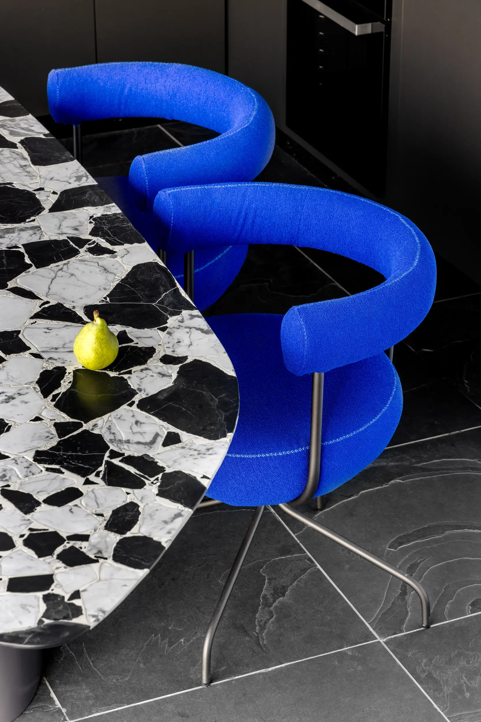 Poltrona escultural azul sobre piso marmorizado no Apto Prisma, design contemporâneo do Studio Guilherme Garcia.