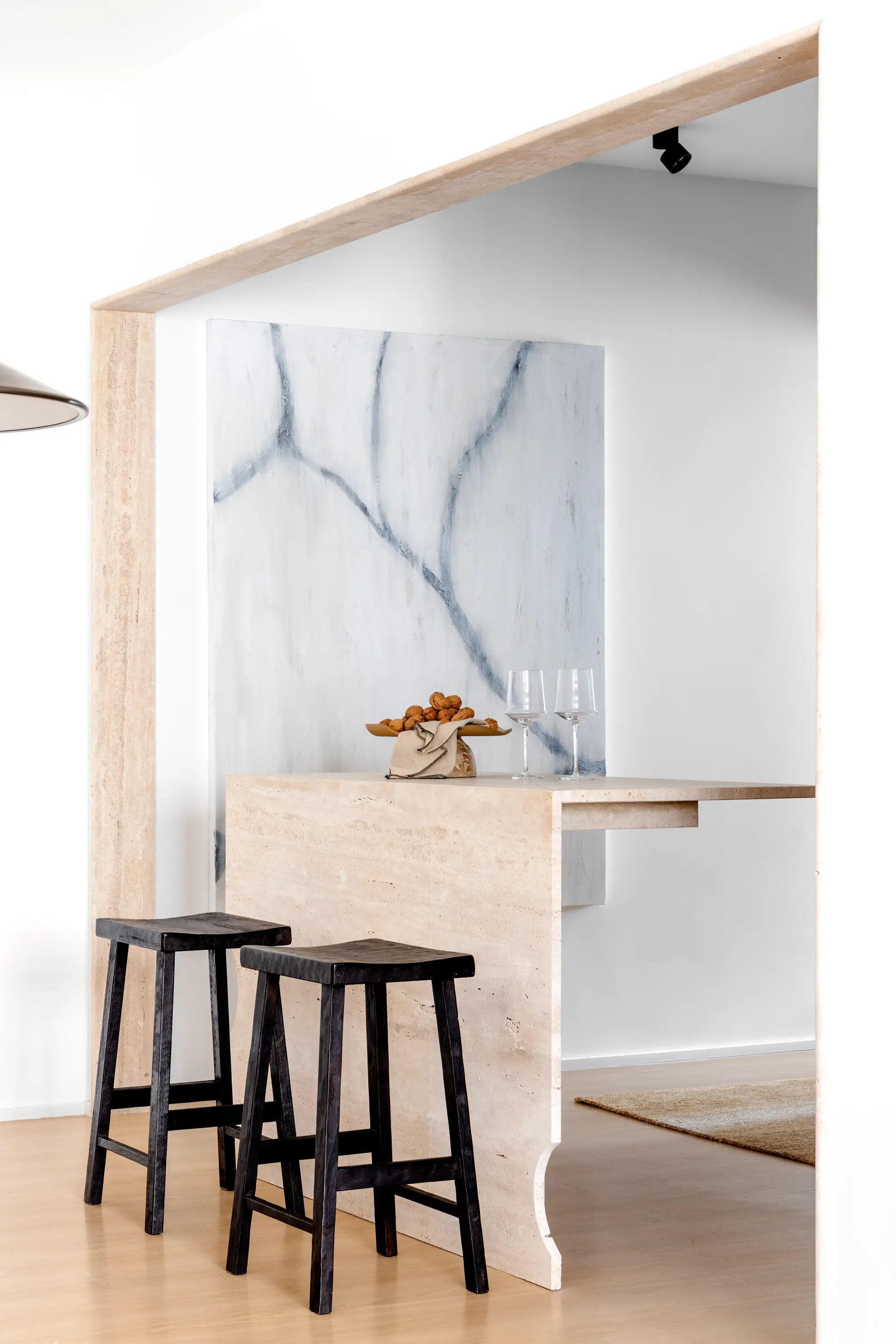 Detalhe da ilha em pedra com banquetas pretas e parede em mármore ao fundo, projeto Lab 06 por Studio Guilherme Garcia.