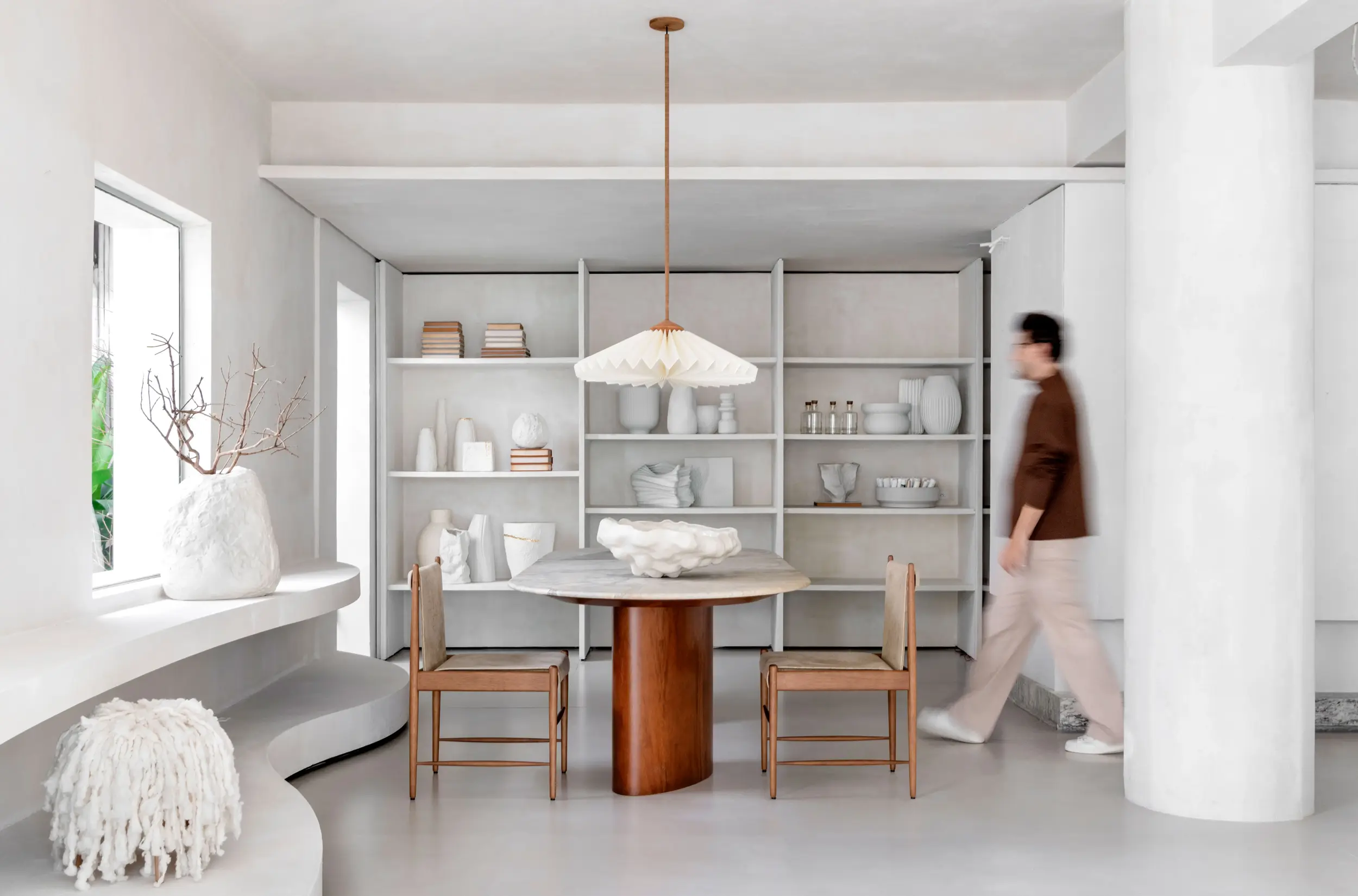 Ambiente interno do projeto Tempo Casa por Studio Guilherme Garcia, com prateleiras esculturais e mesa de jantar em espaço minimalista e sensorial