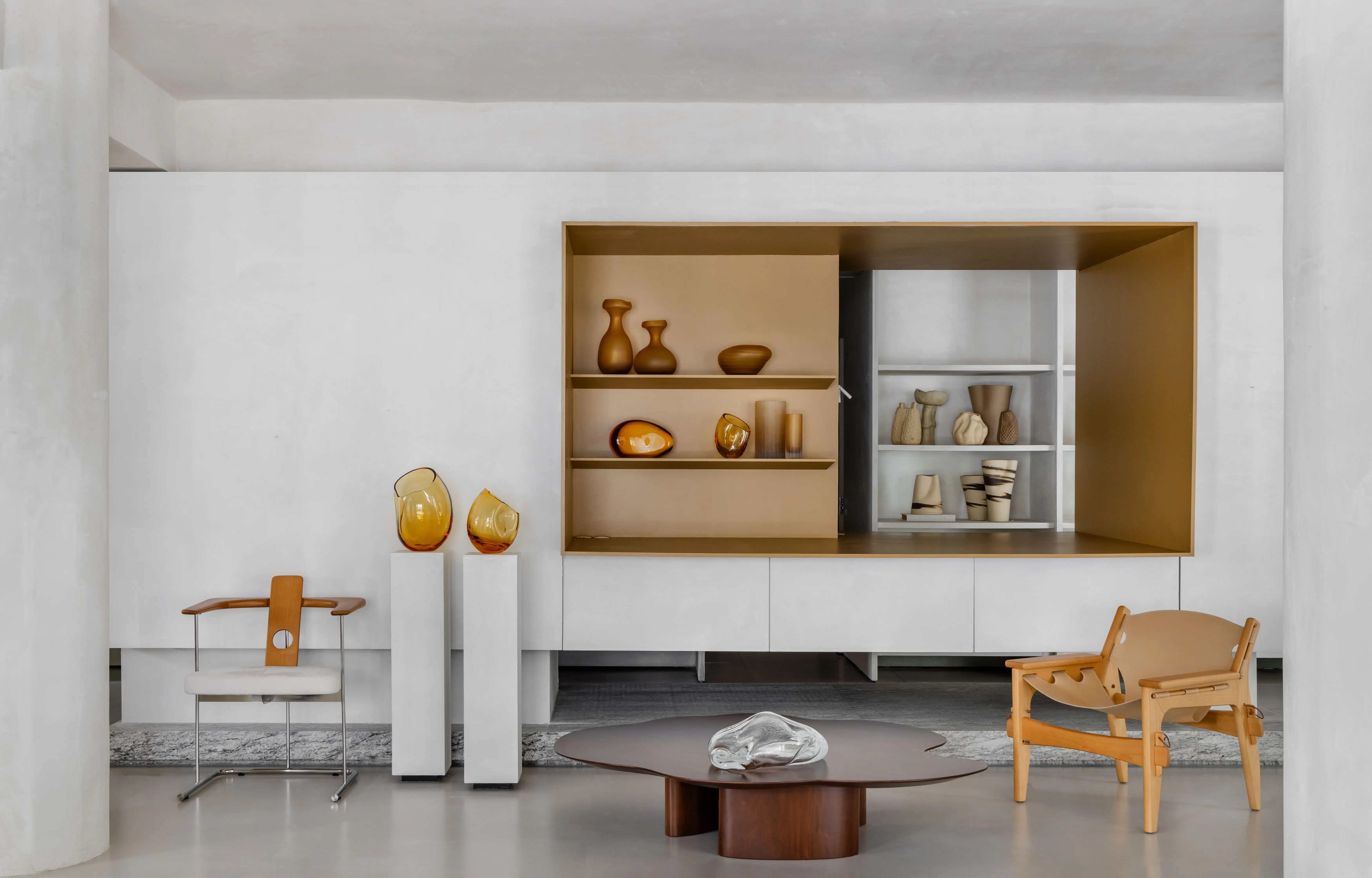 Estante moderna em tons dourado e branco com objetos decorativos, cadeiras de design em madeira clara e mesa de centro minimalista, ambiente contemporâneo do Studio Guilherme Garcia, projeto Tempo Casa