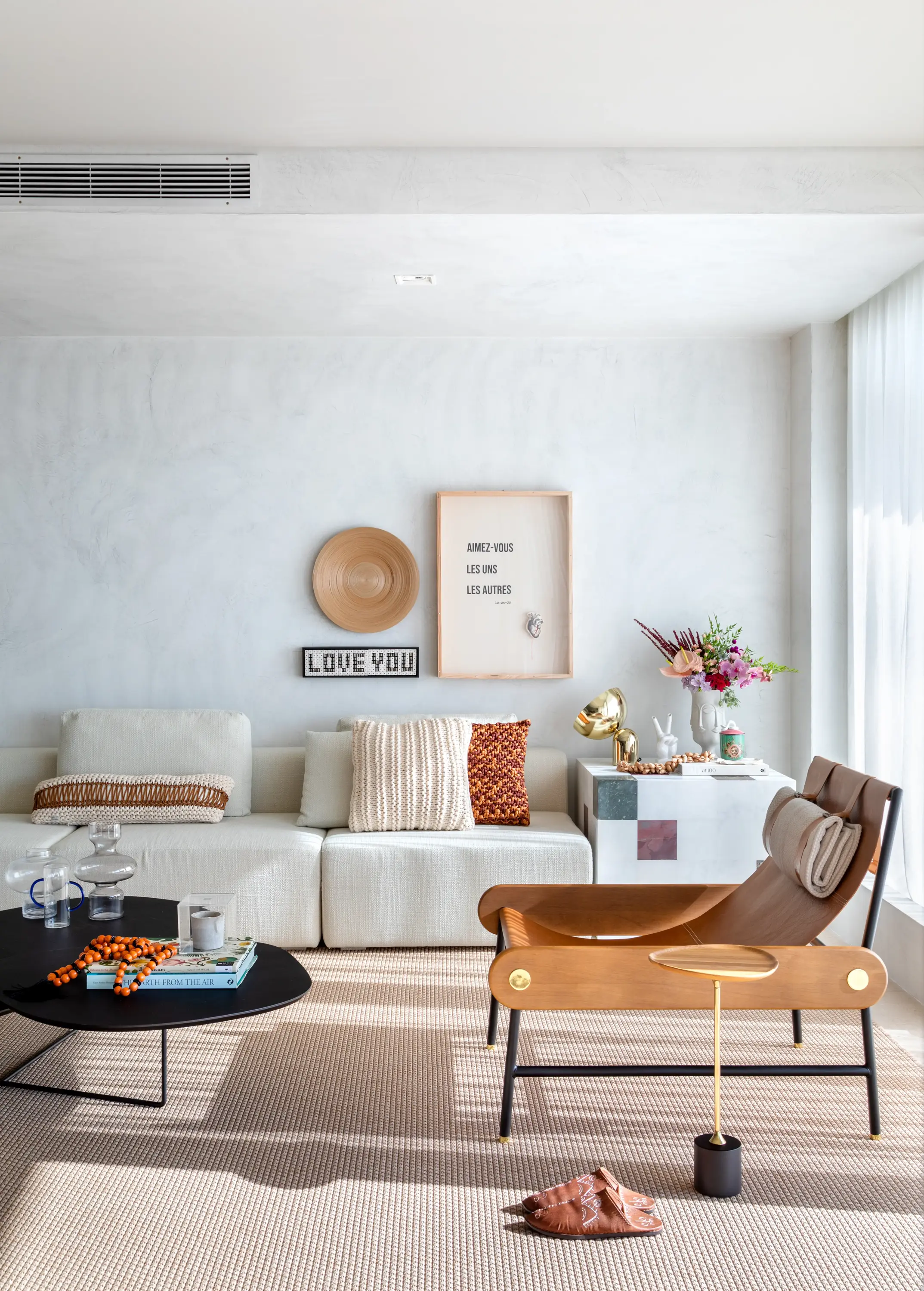 Sala ampla com sofá claro, quadros afetivos e luz natural no Apto Holidays, projeto do Studio Guilherme Garcia.