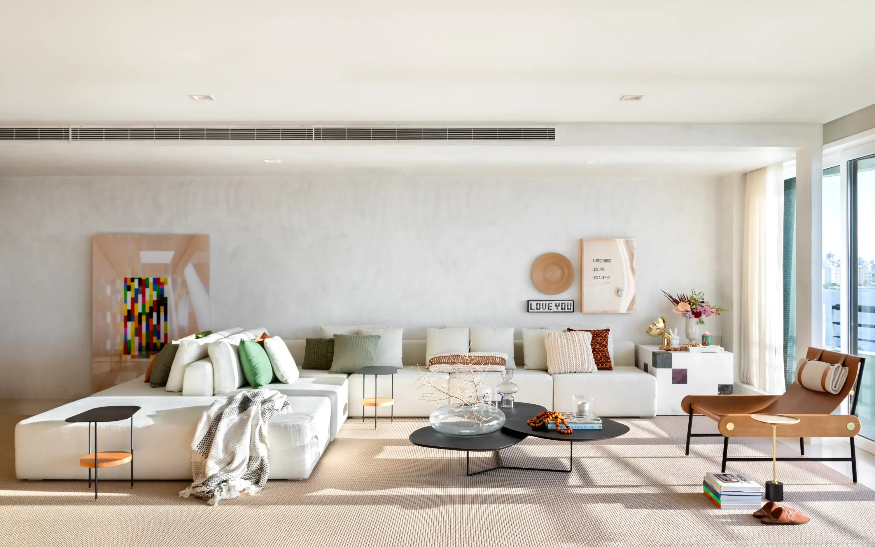 Ambiente principal do Apto Holidays com sofá em tons neutros e décor afetiva sob luz natural, projeto Studio Guilherme Garcia.