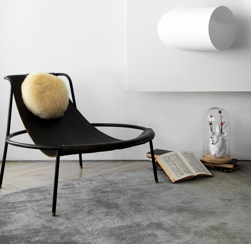Poltrona preta com manta clara e escultura sob redoma de vidro no Studio Guilherme Garcia