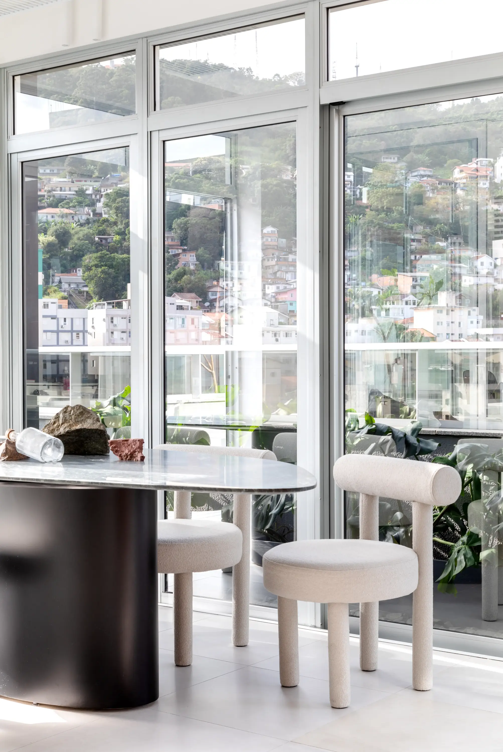 Mesa orgânica e cadeiras minimalistas de tecido bouclé. Vista para a cidade a partir do Escritório SGG com luz natural abundante — projeto por Studio Guilherme Garcia