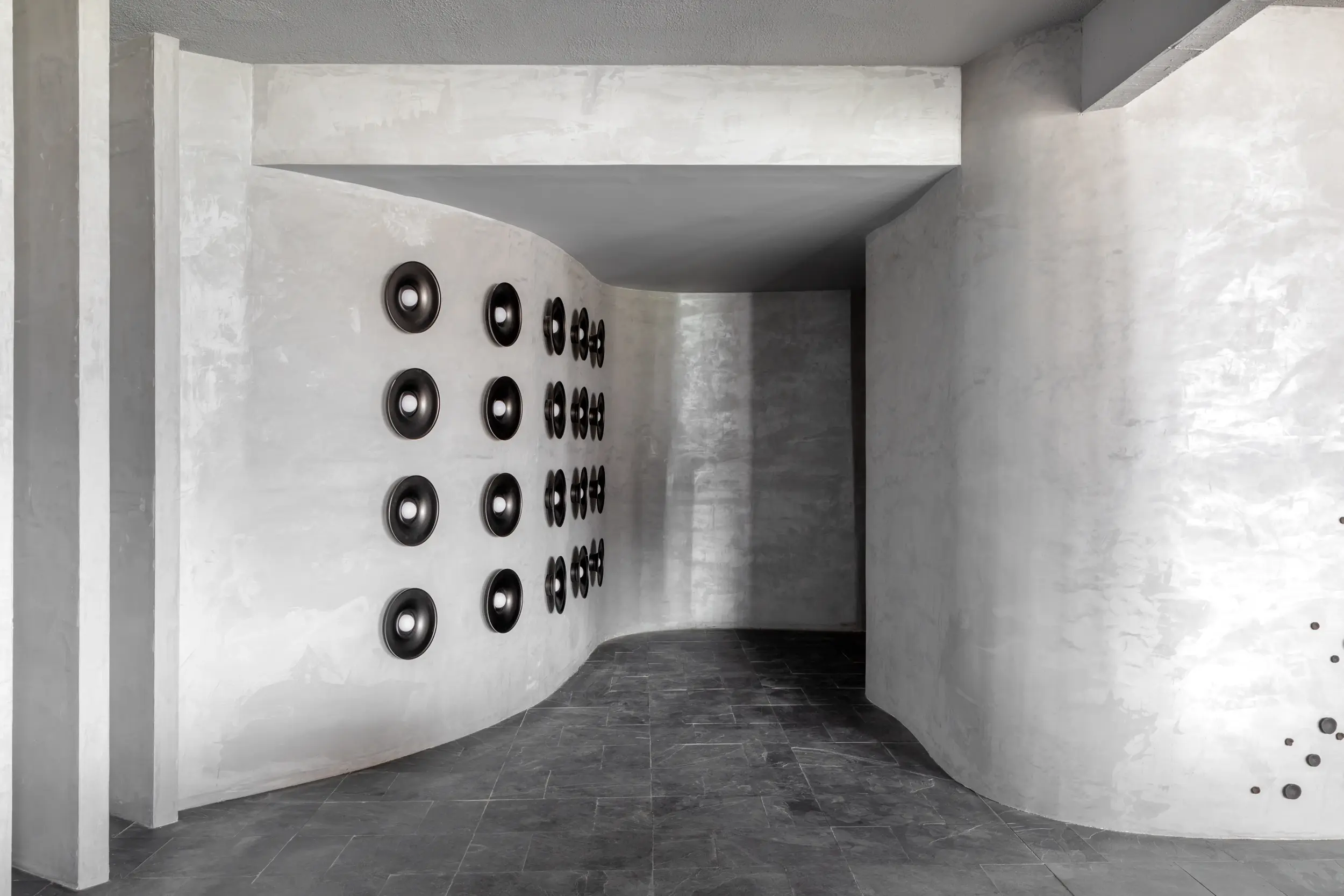 Ambiente brutalista com arte escultórica em parede curva no projeto Estar Origens — Studio Guilherme Garcia