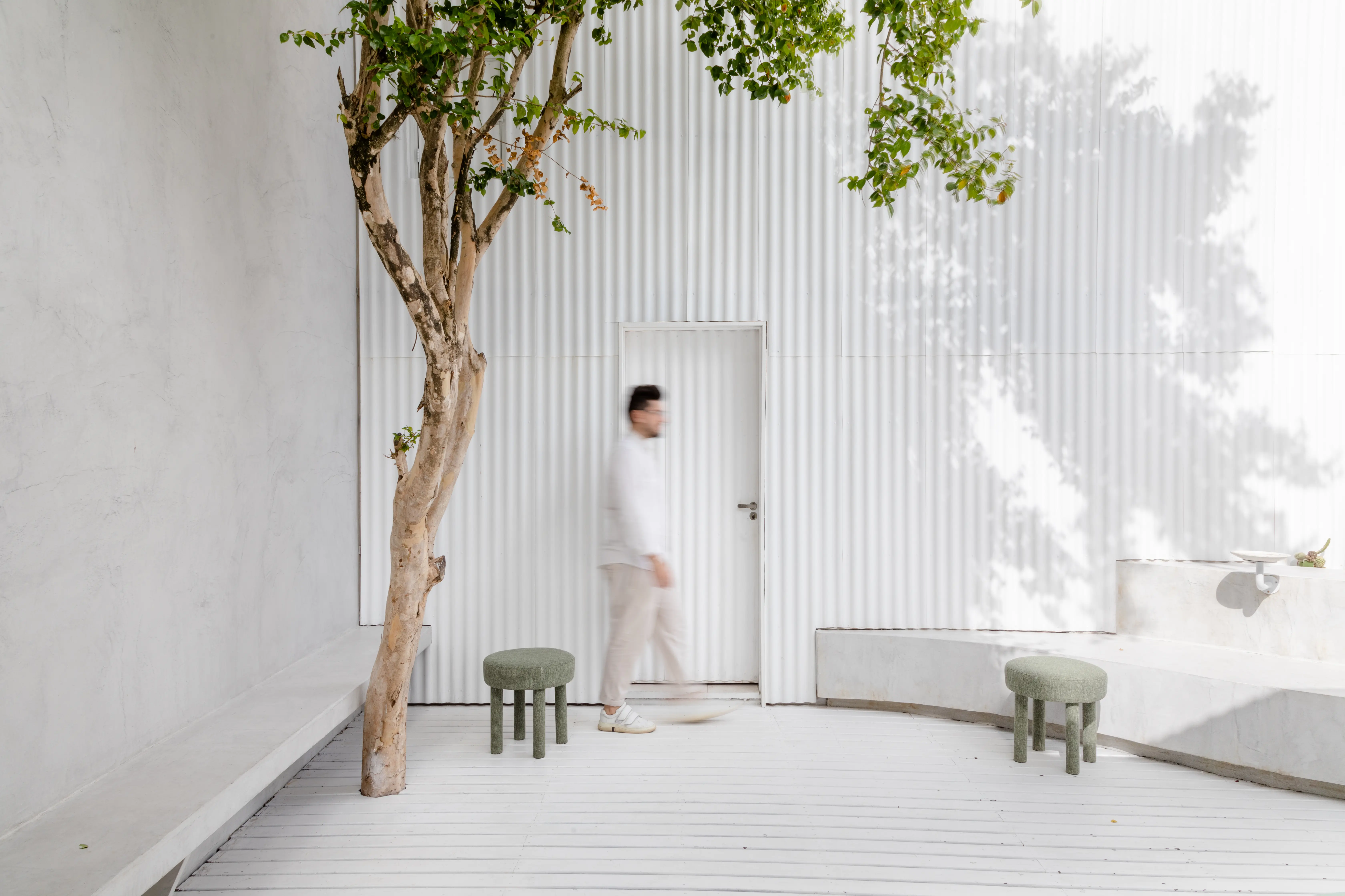 Área externa do Green Blood com árvore, bancos de concreto e revestimento branco ripado em projeto do Studio Guilherme Garcia