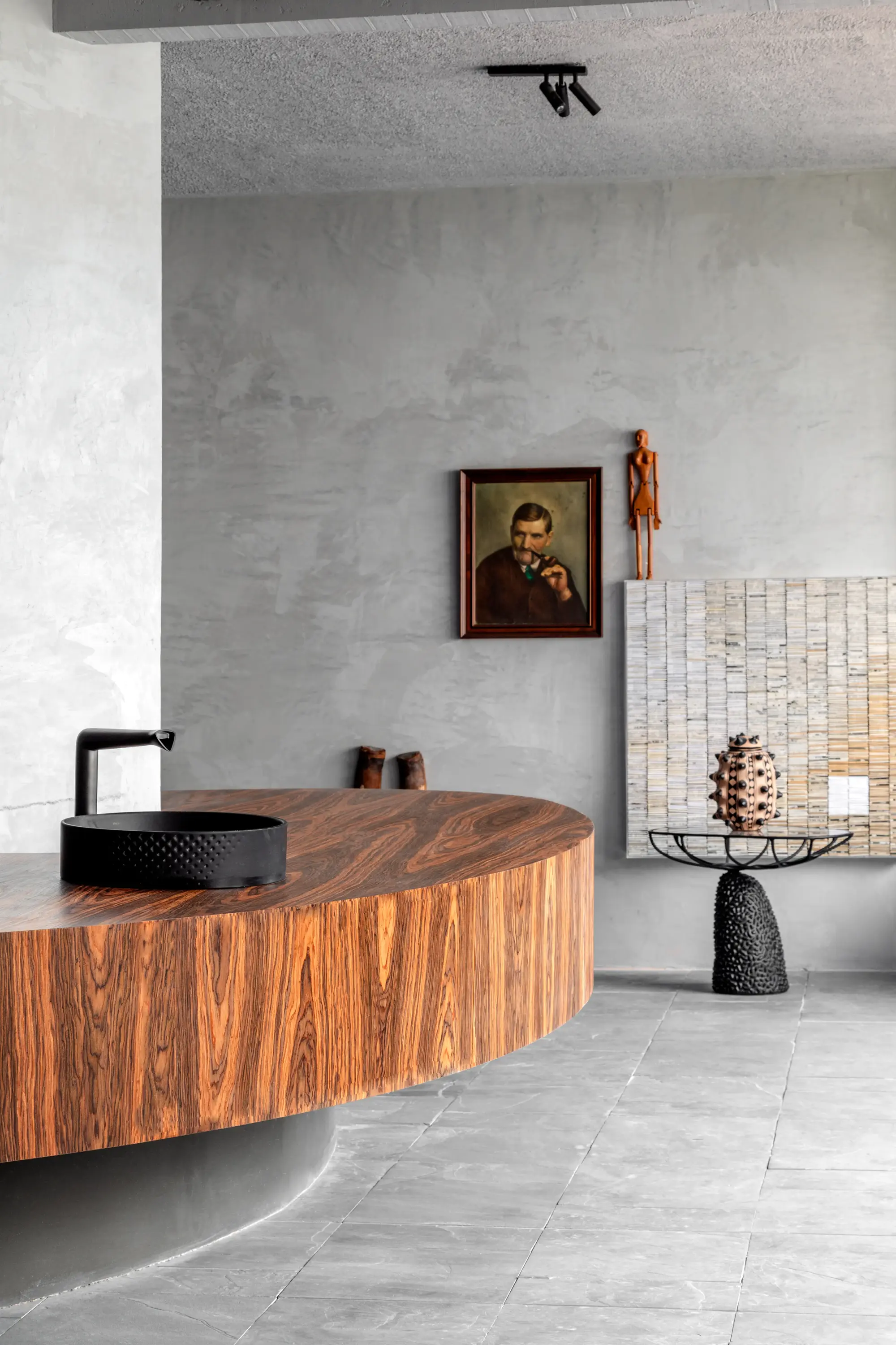 Bancada escultural em madeira natural com parede de concreto e arte sacra — Estar Origens, Studio Guilherme Garcia